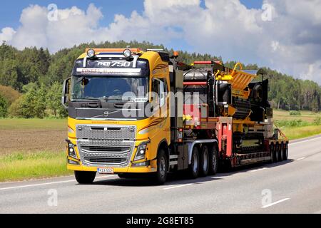 Le camion jaune Volvo FH16 Kosken Autokeskus transporte le destructeur de déchets Tana Shark sur une remorque surbatée sous forme de charge large. Route 52, Salo, Finlande. 11 juin 2021. Banque D'Images