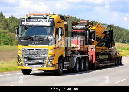 Le camion jaune Volvo FH16 Kosken Autokeskus transporte le destructeur de déchets Tana Shark sur une remorque surbatée sous forme de charge large. Route 52, Salo, Finlande. 11 juin 2021. Banque D'Images