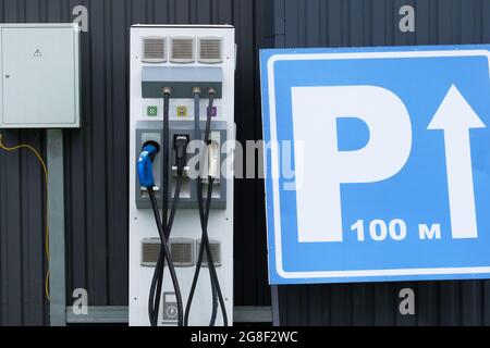 Concept de transport écologique. Station de charge électrique de voiture installée près d'une clôture métallique près du parking. Banque D'Images