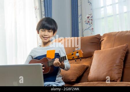 Le garçon apprend à jouer le ukulele avec des leçons en ligne. Banque D'Images