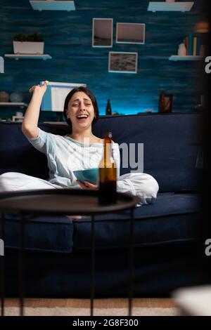Femme intéressée mangeant du pop-corn et regardant des séries de divertissement à la télévision. Maison concentrée seule la nuit avec visage surpris regardant le suspense film assis sur un canapé confortable intéressé. Banque D'Images