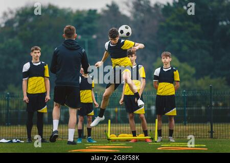 Les jeunes joueurs de football entrainement des têtes de balle les jeunes joueurs sautent à la hauteur et au ballon de tête. Entraîneur entraîneur junior club de football pour jeunes. Équipement d'entraînement de football Banque D'Images