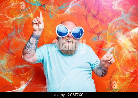 Gras heureux homme avec la barbe, tatouages et lunettes de soleil danse la musique Banque D'Images