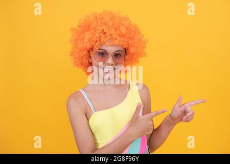 enfant portez des lunettes de soleil et un maillot de bain. jeune fille avec un doigt de pointage de cheveux orange. Banque D'Images