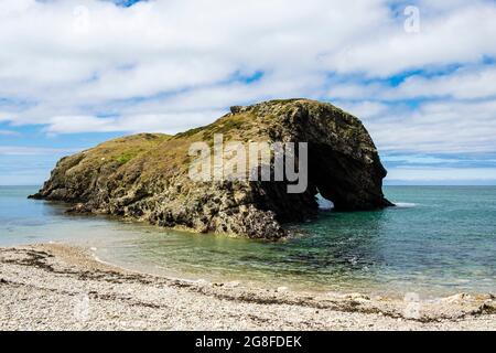 Plage de galets et Ynys y Fydlyn rock Island avec arche à marée haute près de Carmel Head sur la côte. Île d'Anglesey, nord du pays de Galles, Royaume-Uni, Grande-Bretagne Banque D'Images