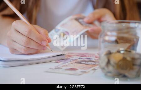 Pièces pot, Nouveau plastique dix et vingt livre sterling note dans les mains de femme faisant des notes dans le bloc-notes. Concept de crise et d'épargne. La finance britannique est un peu plus économique Banque D'Images