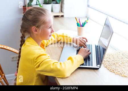 Blanche blonde école fille, taper sur un clavier d'ordinateur portable, faire des devoirs, blogging, chat, regarder des pages de médias sociaux ou jouer. E-learning, retour Banque D'Images