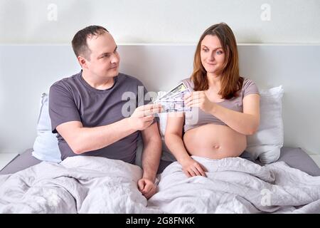 Un homme donne de l'argent à une femme enceinte en dollars américains. Le mari donne à sa femme des factures d'argent pendant sa grossesse Banque D'Images