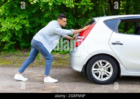 Homme arabe poussant une voiture brisée, vue latérale Banque D'Images
