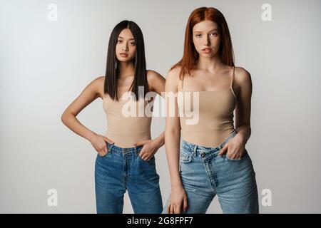 Deux jeunes femmes multiethniques se posant ensemble sur fond de mur gris Banque D'Images