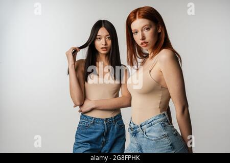 Deux jeunes femmes multiethniques se posant ensemble sur fond de mur gris Banque D'Images