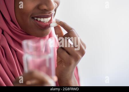 Femme musulmane noire dans le hijab tenant un verre d'eau et prenant la pilule Banque D'Images