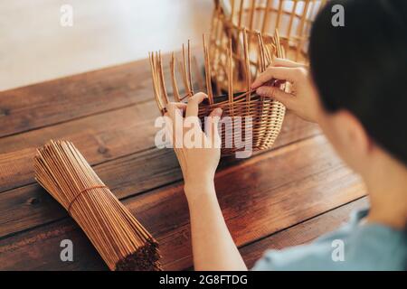 Femme tisse un panier de tubes en papier sur une table en bois. Banque D'Images