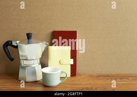 Cafetière, tasse, carnet sur bureau en bois. Fond de mur brun. Espace de travail Banque D'Images