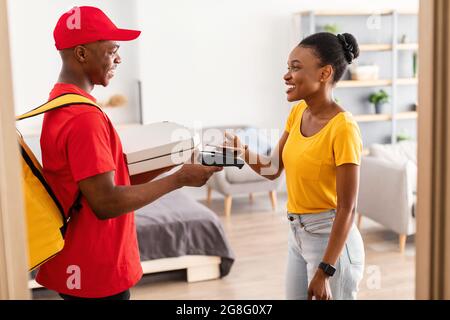 African Female payant Courier pour Pizza avec téléphone mobile à l'intérieur Banque D'Images