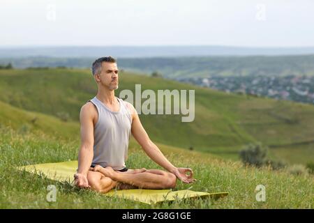 Yoga dans la nature. Un barbu pas jeune homme pratique la méditation de yoga assis dans une position de lotus sur l'herbe sur la nature d'été. Banque D'Images