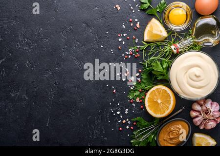 Sauce mayonnaise maison et ingrédients citron, œufs, huile d'olive, épices et herbes, fond noir. Cuisine de fond. Vue de dessus. Banque D'Images