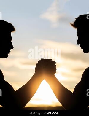 Deux hommes luttant. Comparaison rivalité, vs, défi, force. Coucher de soleil, lever du soleil. Silhouette de mains qui rivalisent en force. Rivalité, gros plan Banque D'Images