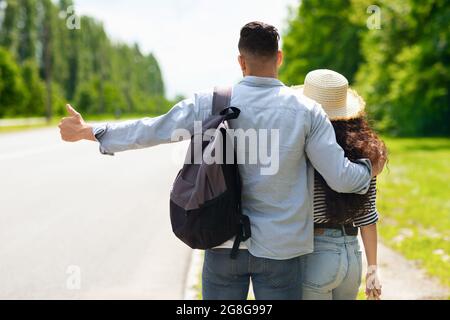 Vue arrière de couple Hitchiking, arrêtant la voiture sur la route Banque D'Images