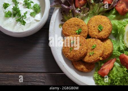 Falafel frais de pois chiches, graines de sésame, épices et herbes, avec salade et une sauce au yaourt sur bois rustique foncé, vue d'en haut, selec Banque D'Images