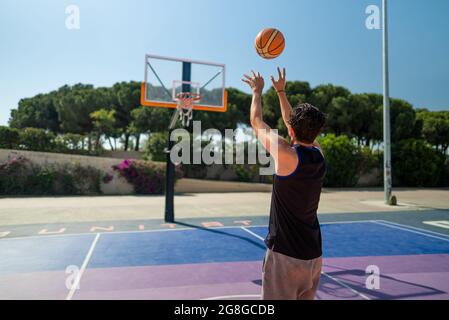 Vue arrière d'un sportif masculin jouant au basket-ball, jetant le ballon sur le terrain de jeu, vue de derrière. Prise de vue de précision Banque D'Images