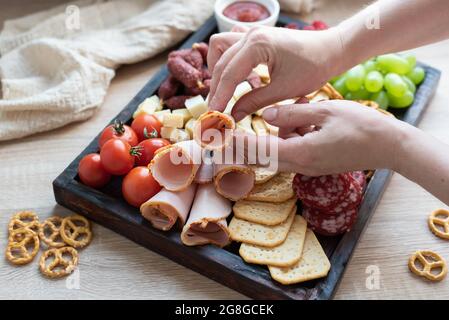 Mains de femmes posant le jambon sur un tableau de charcuterie avec saucisse, fruits et fromage, cuisine de fête, gros plan. Banque D'Images