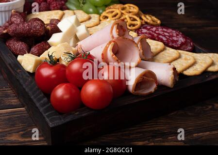 Gros plan sur un plateau de charcuterie avec saucisses, fruits, craquelins et fromage sur fond de bois sombre. Banque D'Images