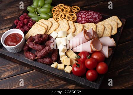 Charcuterie aux saucisses, au fromage et aux fruits sur fond de bois sombre, encas de fête, gros plan. Banque D'Images