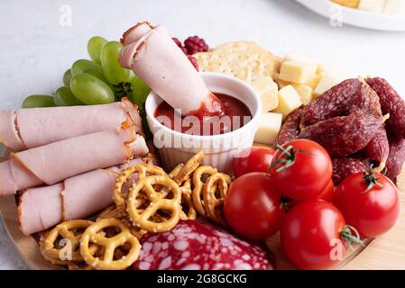 Tranche de jambon dans la sauce sur le plateau de charcuterie avec saucisse, fromage, crackers et fruits, assiettes avec hors-d'œuvre, gros plan. Banque D'Images