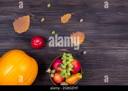 Citrouilles d'orange avec pommes et poires dans un panier avec raisins, noix et feuilles sur une table en bois marron. Vue de dessus Banque D'Images