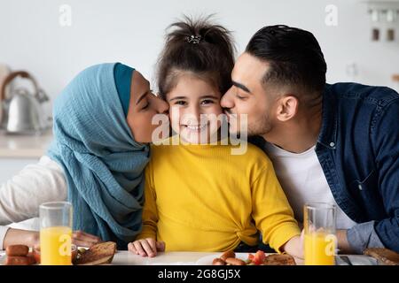 Parents aimant embrasser leur petite fille tout en manger le petit déjeuner dans la cuisine Banque D'Images