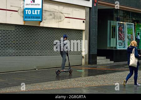 SHEFFIELD. YORKSHIRE DU SUD. ANGLETERRE. 07-10-21. Fargate dans le centre-ville. Un pilote sur un scooter électrique fait son chemin vers le haut de la chaussée humide. Banque D'Images