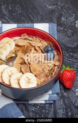 Muesli. Petit déjeuner, alimentation saine et alimentation. Muesli au lait et aux fruits dans une assiette sur un dessus en marbre noir. Main de femme avec une cuillère Banque D'Images