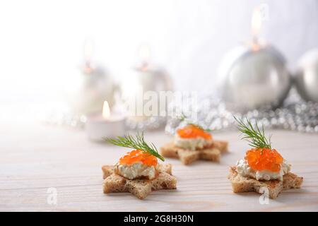 Canapés de vacances de pain grillé en forme d'étoile, caviar crème et rouge avec garniture d'aneth sur une table en bois clair avec bougies et de Noël festif Banque D'Images