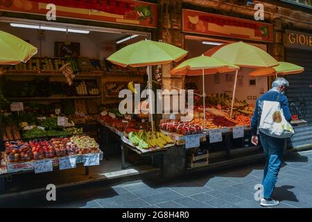 Un homme mûr devant une épicerie avec des fruits frais dans la via San Pietro della Porta, ruelle étroite ('carugio') dans la vieille ville de Gênes, Ligurie Banque D'Images