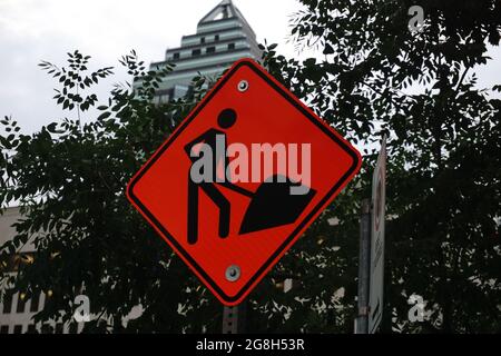 Montréal, QC, Canada - 7-15-2021: Un signe de travaux routiers au centre-ville avec un fond flou d'un gratte-ciel et d'arbres. Banque D'Images