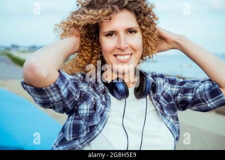 Gros plan Portrait de souriant cheveux bouclés Femme caucasienne avec de grands écouteurs marchant à l'extérieur. Profitez de l'instant et de la musique. Liberté et bonheur Banque D'Images