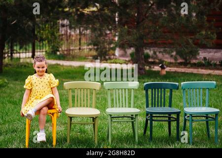 une fille drôle dans une robe jaune est assise sur une rangée de chaises debout sur la pelouse dans le parc et se prépare pour une cérémonie de mariage hors-site sur un chaleureux Banque D'Images