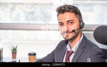 Portrait d'homme d'affaires, agent de centre d'appels portant un micro-casque travaillant avec un ordinateur portable au bureau. Homme en costume consultant le client au téléphone dans la coutume Banque D'Images