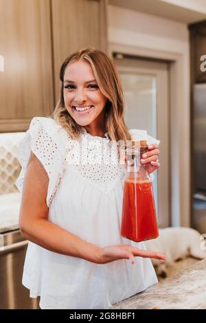 Une femme souriante montre sa carafe fraîchement préparée de jus maison Banque D'Images