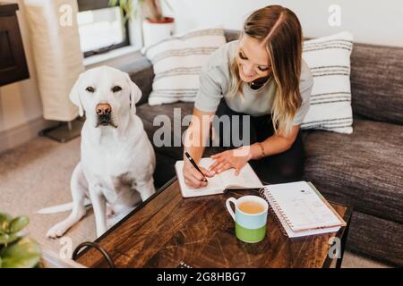 Une femme écrit dans un ordinateur portable tandis que son chien est assis à côté d'elle Banque D'Images