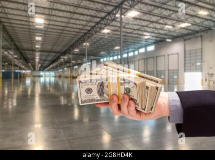 Main mâle tenant des milliers de dollars à l'intérieur de l'entrepôt industriel vide. Banque D'Images