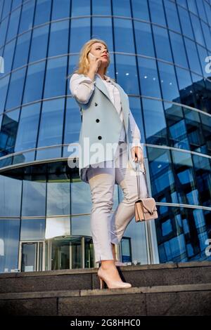 Une jeune femme confiante se tient près du centre d'affaires et parle au téléphone intelligent. Banque D'Images
