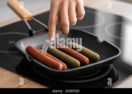 Jeune homme friture de savoureuses saucisses dans la cuisine, en gros plan Banque D'Images