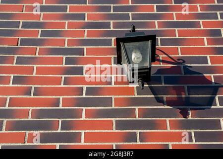 Une lanterne en métal noir avec verre poussiéreux et une lampe à économie d'énergie à l'intérieur, accrochée au mur, projette une ombre sur la droite de la façade, qui est faite Banque D'Images