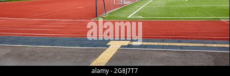 Tapis roulant rouge sur terrain de sport. Paysage de terrain de football avec herbe verte et piste de course Banque D'Images