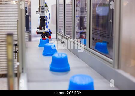 Pots bleus sur le tapis de la machine de moulage par injection plastique avec bras robotisé Banque D'Images