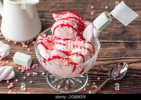 Crème glacée Roma à la fraise, à la banane et à la crème dans un bol en verre avec sauce rouge versée dessus. Banque D'Images