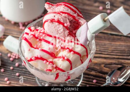 Crème glacée Roma à la fraise, à la banane et à la crème dans un bol en verre avec sauce rouge versée dessus. Banque D'Images