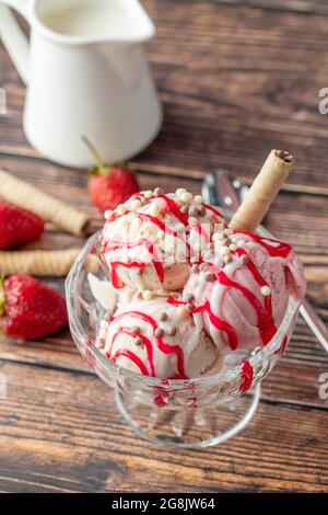 Crème glacée Roma à la fraise, à la banane et à la crème dans un bol en verre avec sauce rouge versée dessus. Banque D'Images